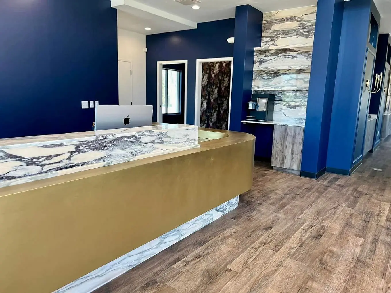 At Holt Orthodontics in Twinsburg, OH, the reception area features a marble and gold front desk, a computer, a marble accent wall, a coffee station, wood flooring, and navy blue walls.