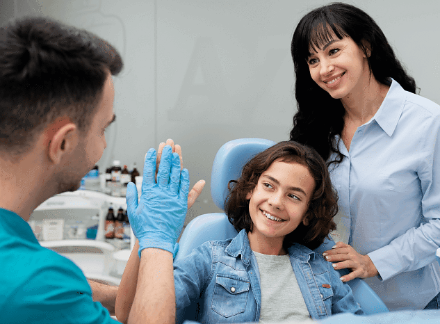 At Holt Orthodontics in Twinsburg, OH, a dentist gives a high five to a smiling child in the dental chair as a supportive woman looks on—highlighting the caring environment provided before and after procedures like jaw surgery.
