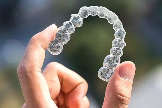 A hand displays a clear Invisalign aligner with an outdoor background, showcasing the type of treatment offered by Holt Orthodontics in Twinsburg, OH.