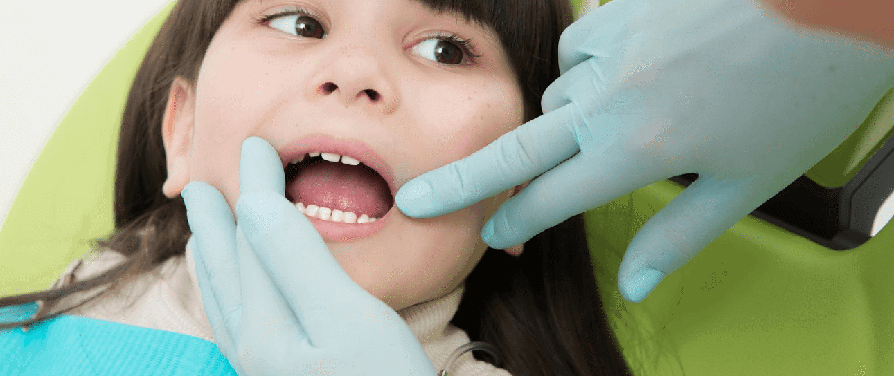 At Holt Orthodontics in Twinsburg, OH, a children’s orthodontist wearing gloves examines a young girl's teeth as she sits comfortably in the dental chair.