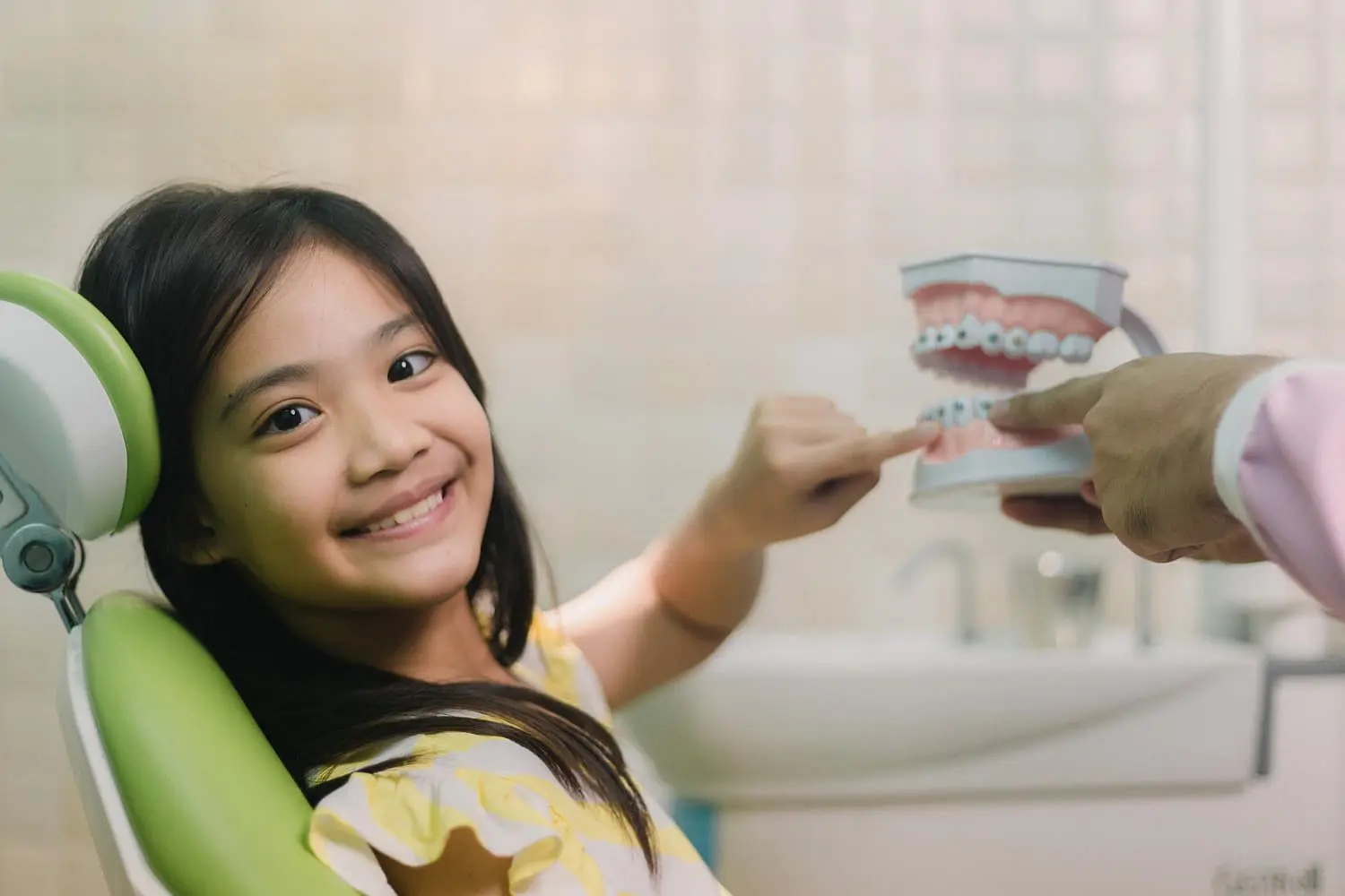 A young girl smiles and points at a dental model held by a children’s orthodontist at Holt Orthodontics in Twinsburg, OH.