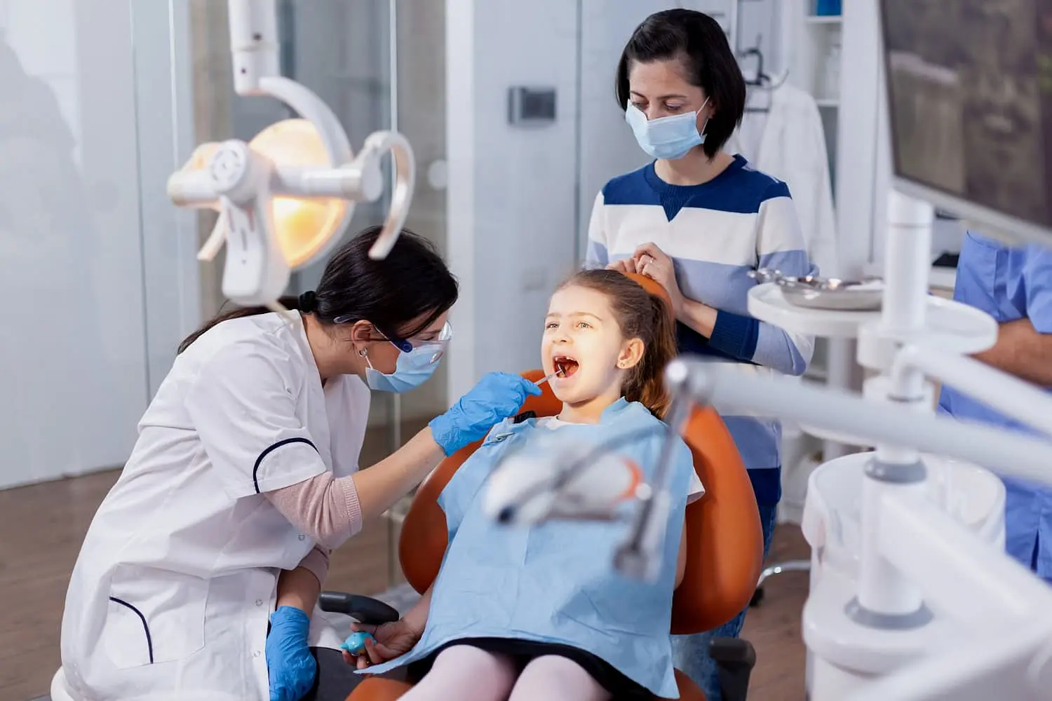 At Holt Orthodontics in Twinsburg, OH, a children’s orthodontist examines a young girl’s teeth in the clinic as her masked mother stands nearby.