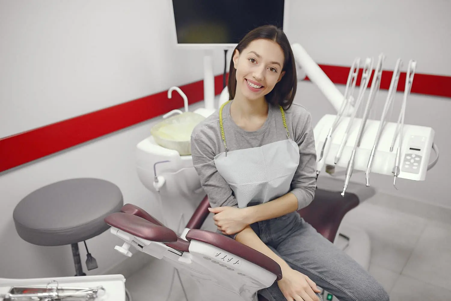 A patient with metal braces sits smiling in a modern dental clinic at Holt Orthodontics in Twinsburg, OH, wearing a dental bib with equipment visible.
