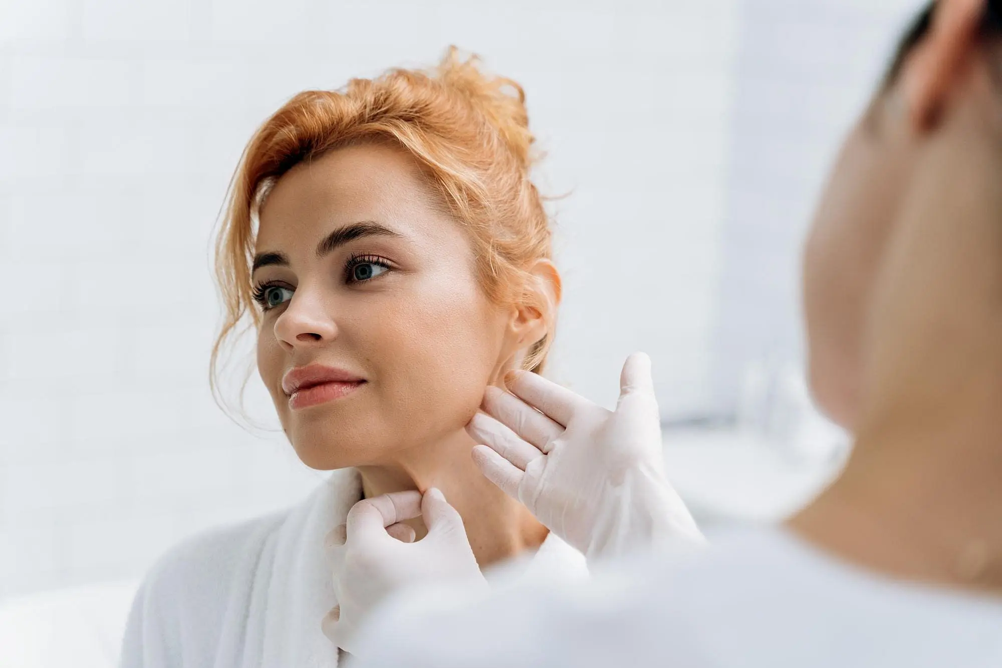 At Holt Orthodontics in Twinsburg, OH, a healthcare professional wearing gloves examines a woman's neck in a clinical setting, possibly assessing her for jaw surgery.