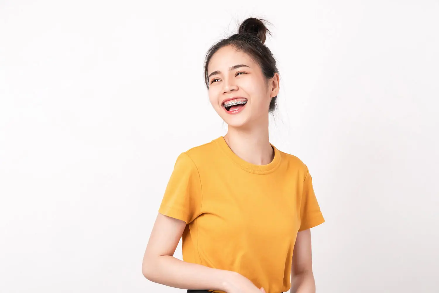 A young woman in a yellow t-shirt, smiling with adult braces, looks slightly to the side against a plain white background at Holt Orthodontics in Twinsburg, OH.