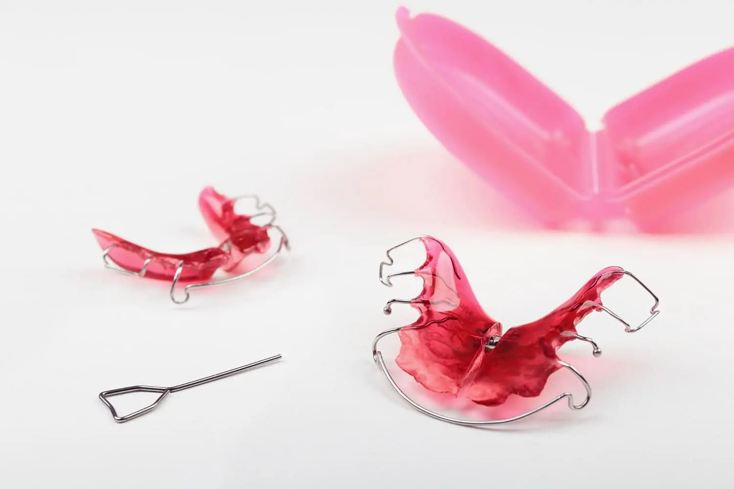 Displayed on a white surface are two pink dental retainers with metal wires, a small adjustment tool, and an open pink plastic case—ideal functional appliances for children recommended by Holt Orthodontics in Twinsburg, OH.