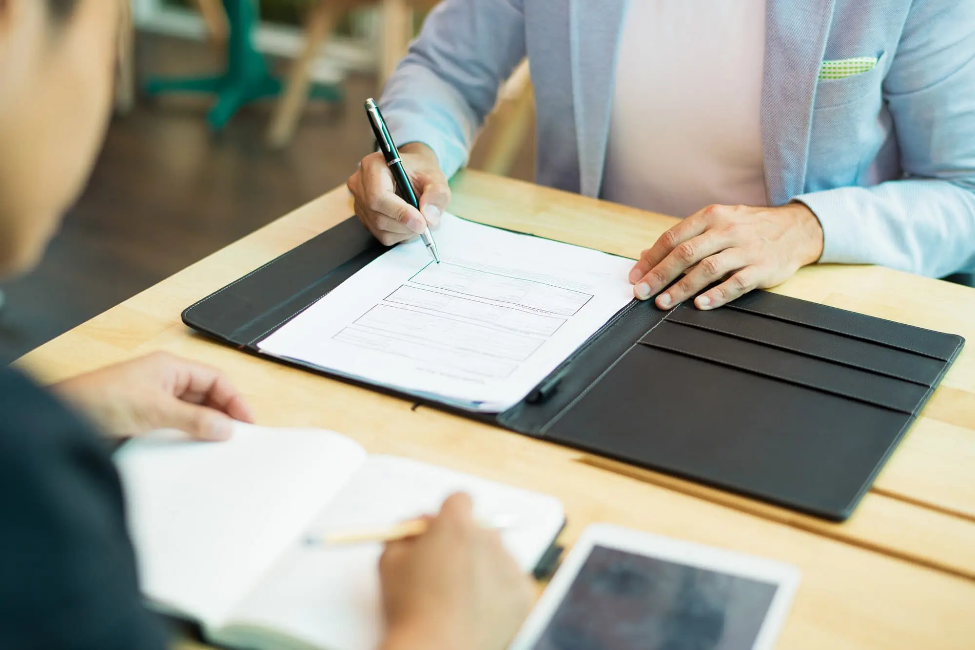 At Holt Orthodontics in Twinsburg, OH, two people sit at a wooden table—one completing an orthodontic insurance plans form on a clipboard, while the other takes notes in a notebook with a tablet nearby.