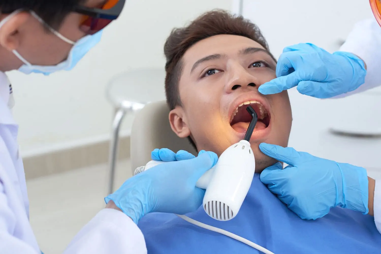 At Holt Orthodontics in Twinsburg, OH, a dentist wearing gloves uses dental tools to examine a patient's mouth for signs of tongue thrust as an assistant holds a nearby device.