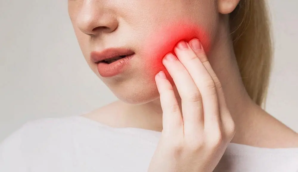 Experiencing jaw or mouth discomfort, as shown by a person touching their cheek with a red spot, many seek relief at Holt Orthodontics in Twinsburg, OH, exploring options like Invisalign vs Braces.