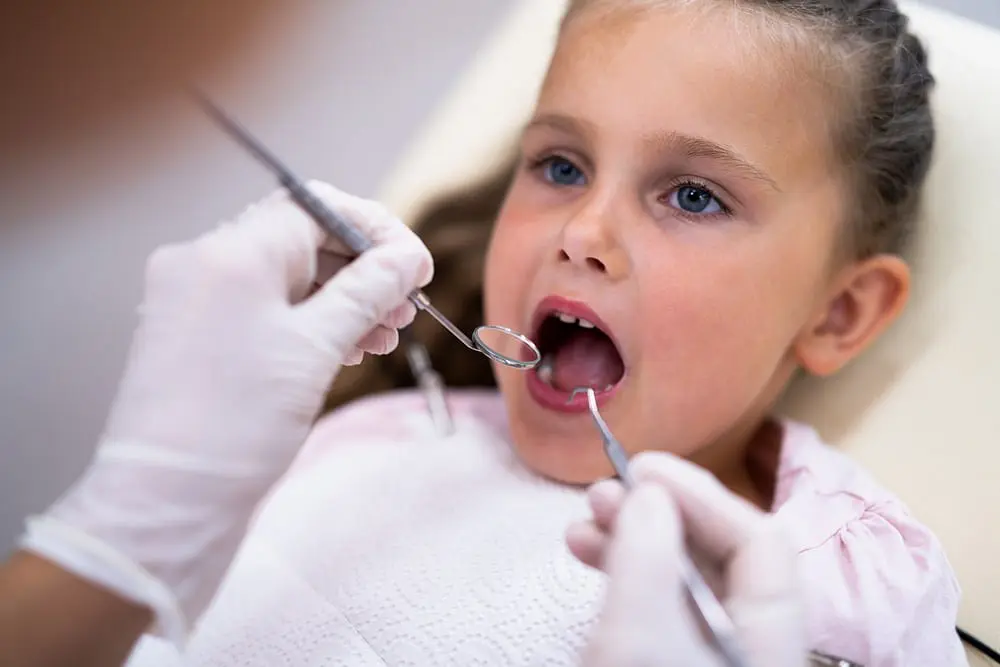 At Holt Orthodontics in Twinsburg, OH, a dentist examines a young girl's teeth for signs of tongue thrust as she sits in the dental chair with her mouth open.