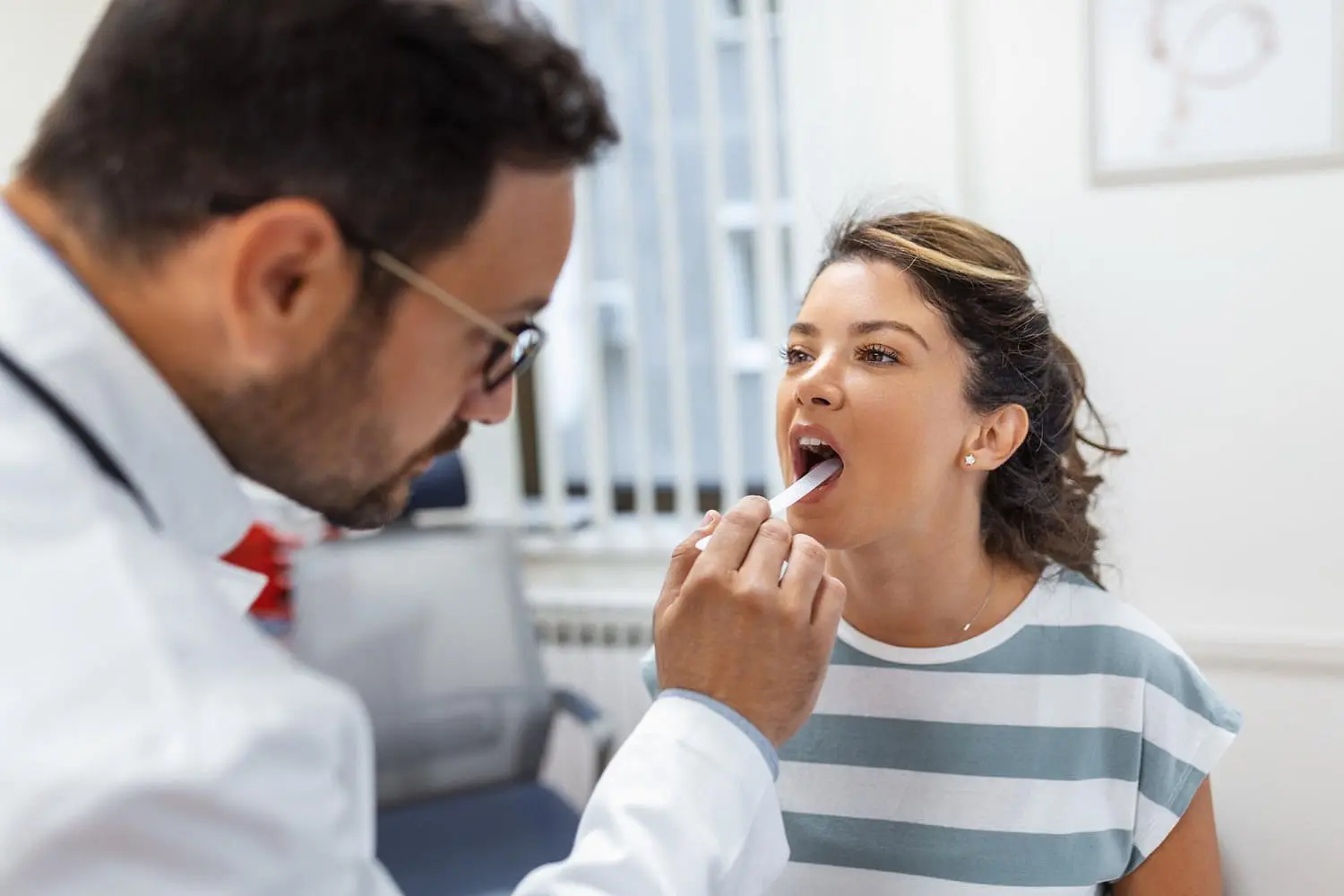 During a medical check-up at Holt Orthodontics in Twinsburg, OH, a doctor uses a tongue depressor to carefully examine a patient's throat for signs of an underbite.
