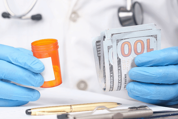 At Holt Orthodontics in Twinsburg, OH, a person wearing blue medical gloves holds an empty prescription bottle and several $100 bills, with a stethoscope and pen nearby—symbolizing healthcare expenses or selecting an Invisalign Payment Plan.