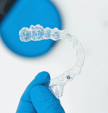 A gloved hand holds a clear dental aligner, with a blurred blue circle in the background—ideal imagery for those considering an Invisalign Payment Plan at Holt Orthodontics in Twinsburg, OH.