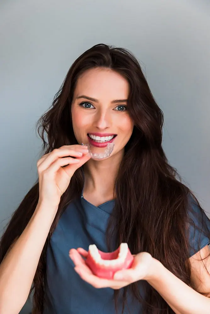 At Holt Orthodontics in Twinsburg, OH, a woman with long brown hair smiles as she fits an Invisalign clear aligner onto her teeth using a dental model.