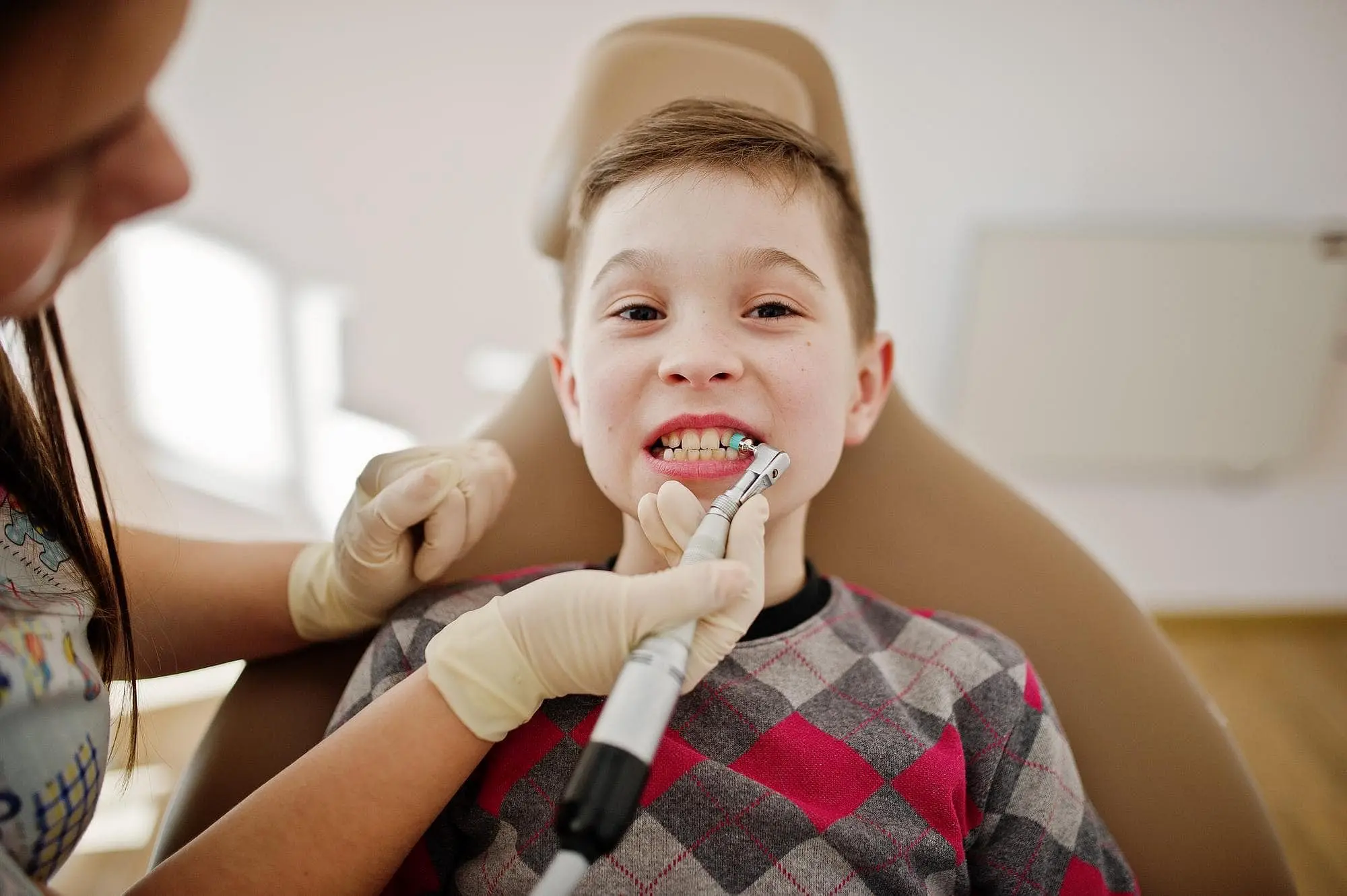 At Holt Orthodontics in Twinsburg, OH, a children’s orthodontist in gloves uses dental tools to clean a child’s teeth as he sits in the dentist’s chair.