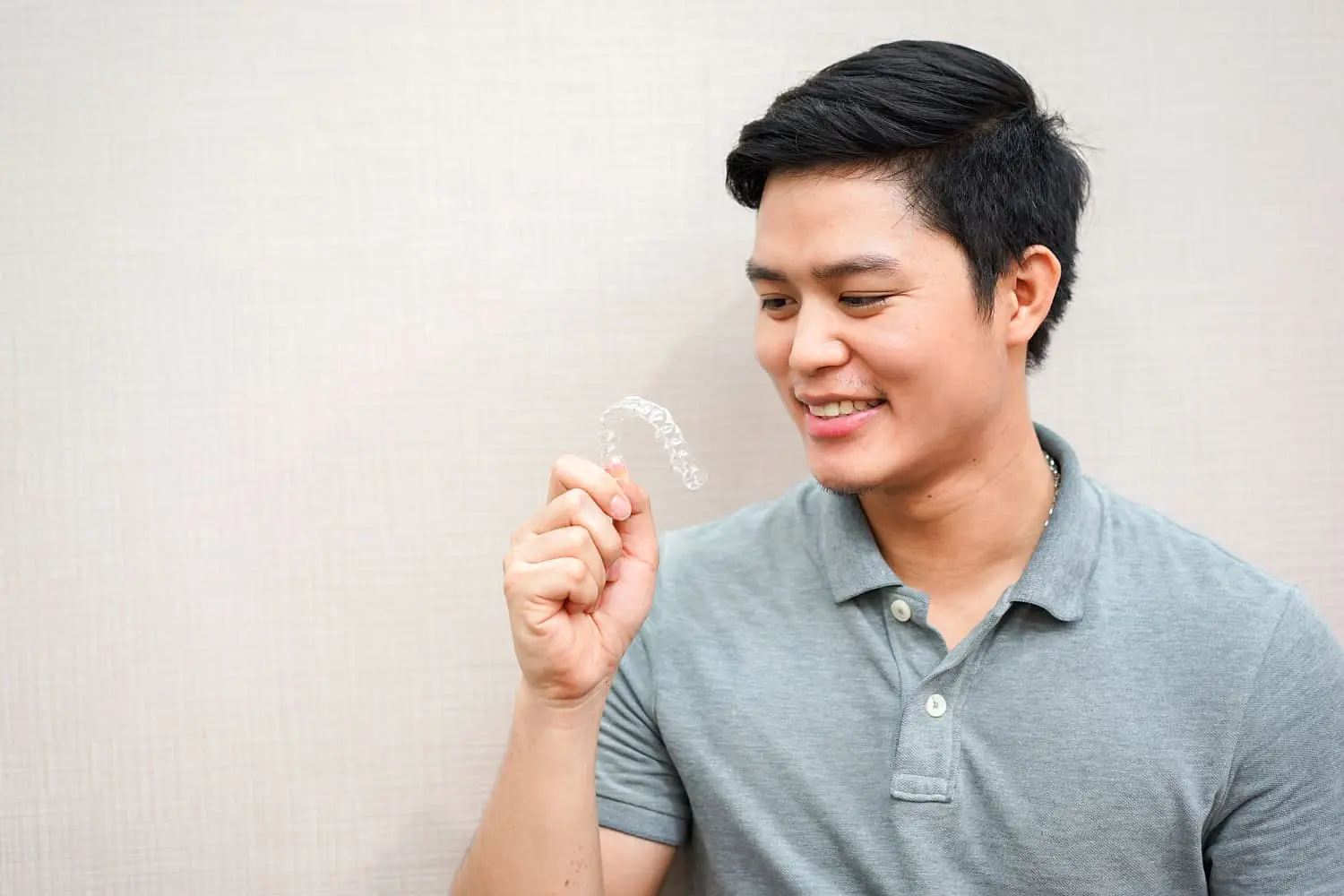 At Holt Orthodontics in Twinsburg, OH, a man in a gray polo shirt holds and examines a clear dental aligner, highlighting the benefits of affordable Invisalign against a simple light-colored background.