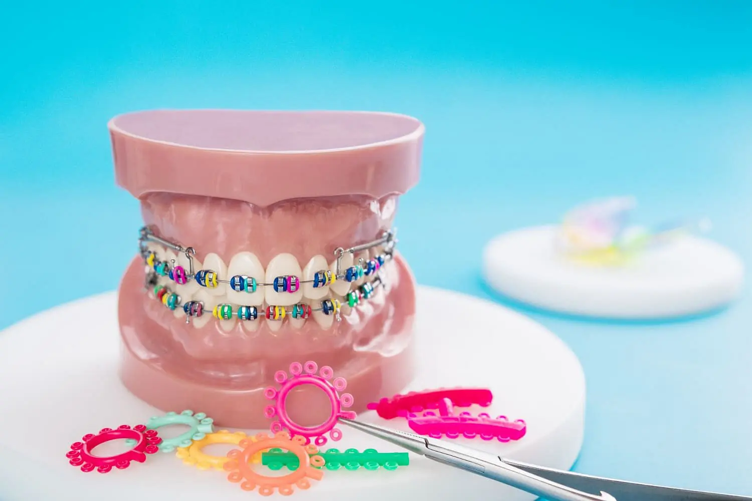 A dental model with metal braces and colorful bands, along with orthodontic elastics and tools, is displayed on a white surface with a blue background at Holt Orthodontics in Twinsburg, OH.