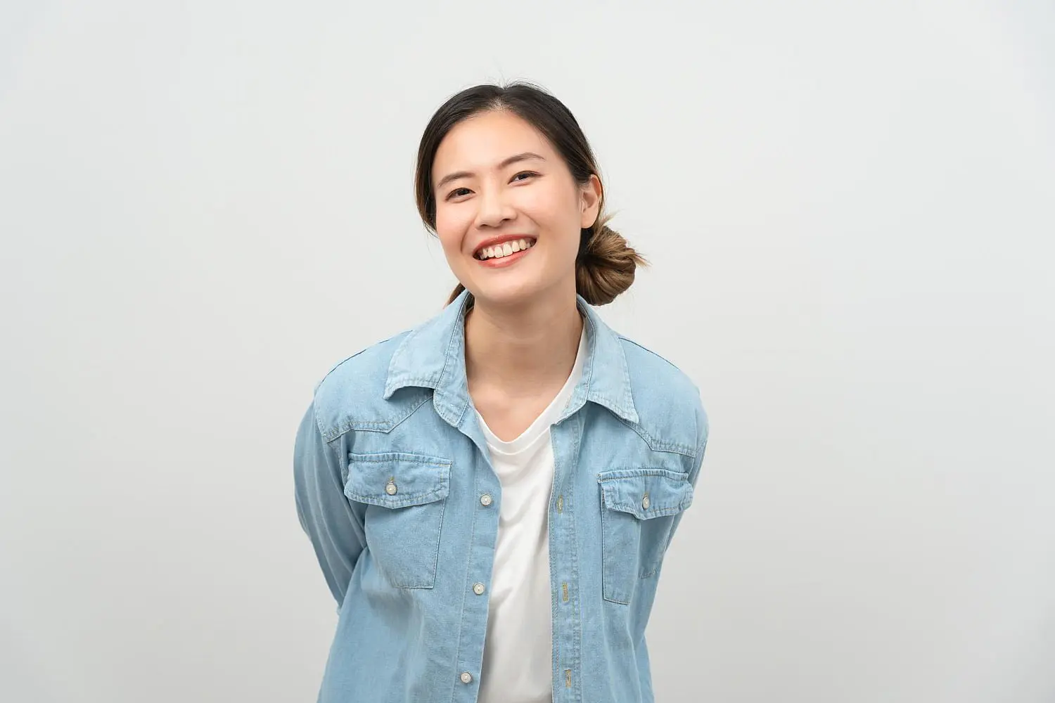 A young woman with dark hair in a ponytail confidently smiles, showing her Invisalign aligners in a light blue denim shirt and white top. This reflects the quality care provided by Holt Orthodontics in Twinsburg, OH.