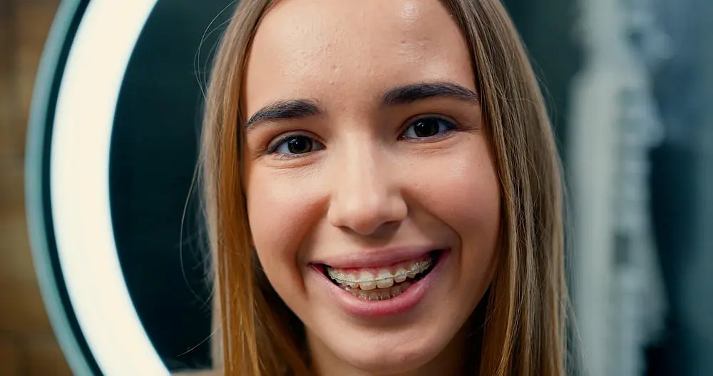 At Holt Orthodontics in Twinsburg, OH, a young person with long brown hair and clear braces smiles at the camera, illuminated by a circular light in the background.