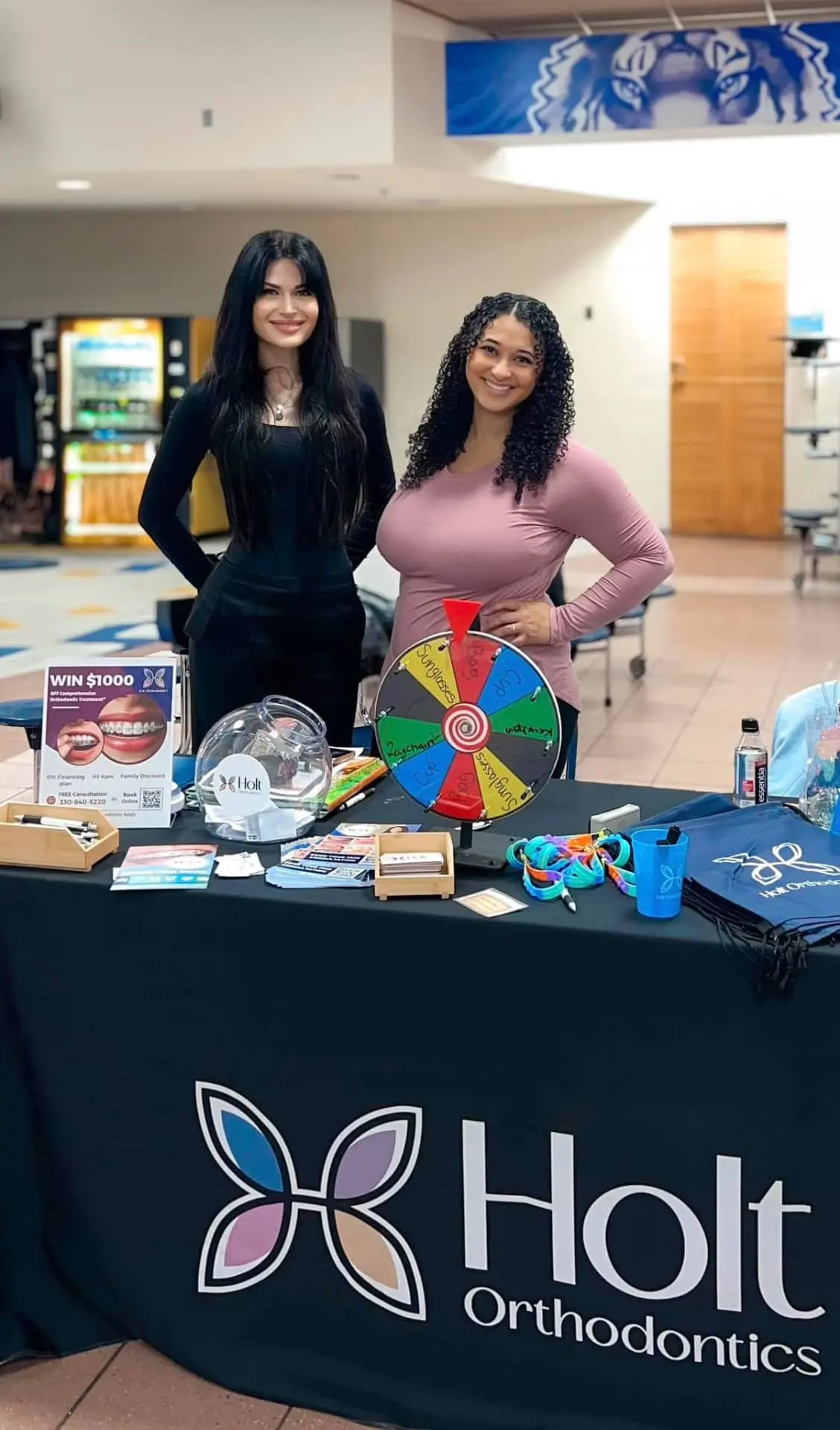 At a community indoor event in Twinsburg, OH, two women represent Holt Orthodontics behind a display table with a prize wheel, brochures, and promotional items for Dr. Shalise Holt’s practice.