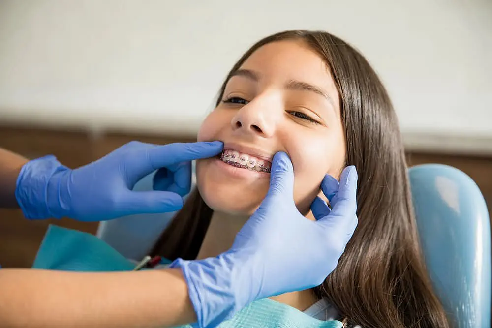 At Holt Orthodontics in Twinsburg, OH, a children’s orthodontist in blue gloves examines a young patient’s traditional braces.