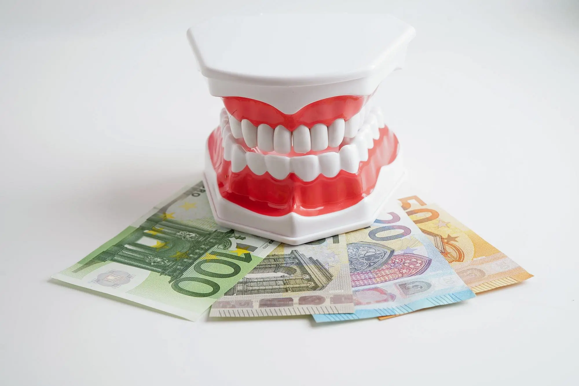 A model of human teeth is displayed on euro banknotes (20, 50, and 100) against a white background, illustrating the value of orthodontic insurance plans at Holt Orthodontics in Twinsburg, OH.