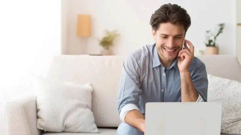 A man relaxes on a sofa in a bright, modern living room, smiling as he browses the FAQ section of Holt Orthodontics in Twinsburg, OH on his laptop.