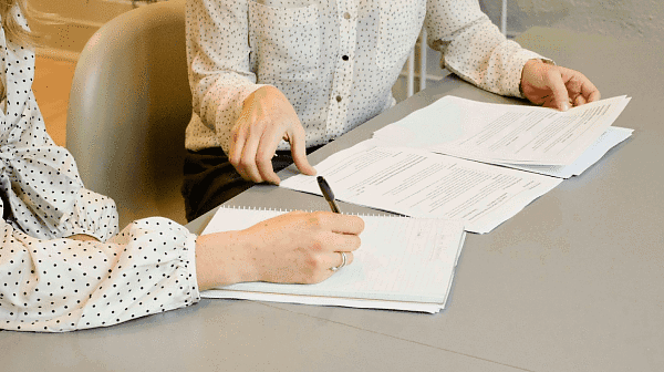 At Holt Orthodontics in Twinsburg, OH, two people sit at a table reviewing documents—one writing in a notebook while the other points to printed papers—as they discuss whether Invisalign is covered by insurance.