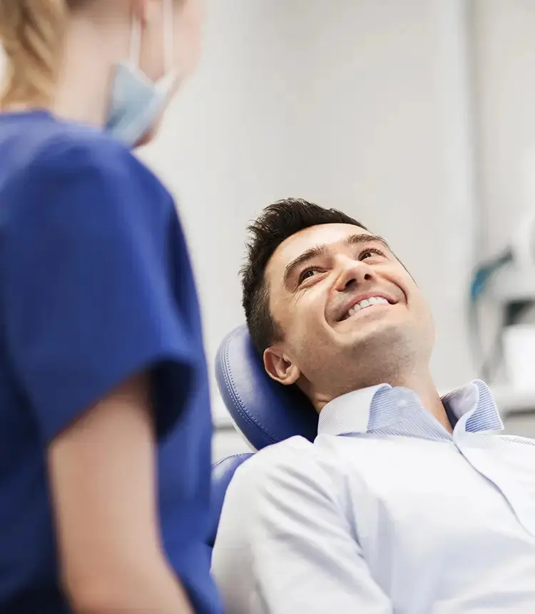 At Holt Orthodontics in Twinsburg, OH, a man smiles from the dental chair while a masked dental professional in blue scrubs discusses available patient resources with him.