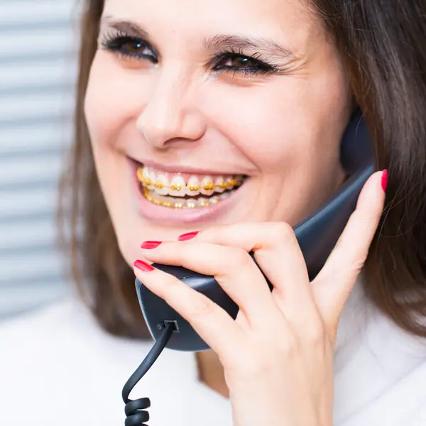 A woman smiles hold telephone with gold brace from top-rated orthodontist at Holt Orthodontics in Twinsburg, OH.