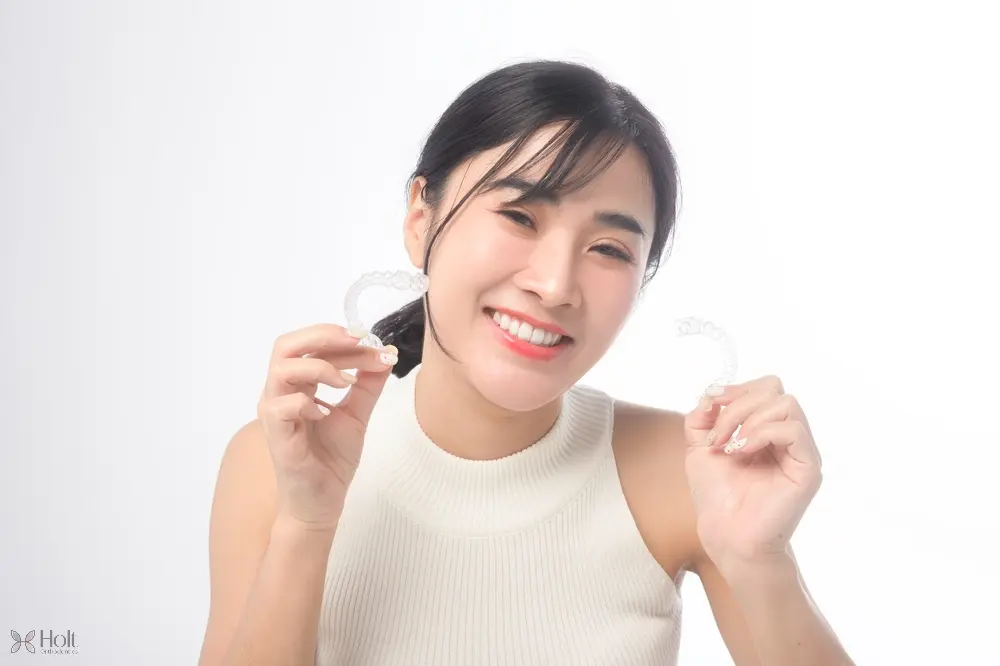 young smiling woman holding invisalign clear aligners white dental studio - Can Invisalign Fix Overbite in Twinsburg, OH.  
