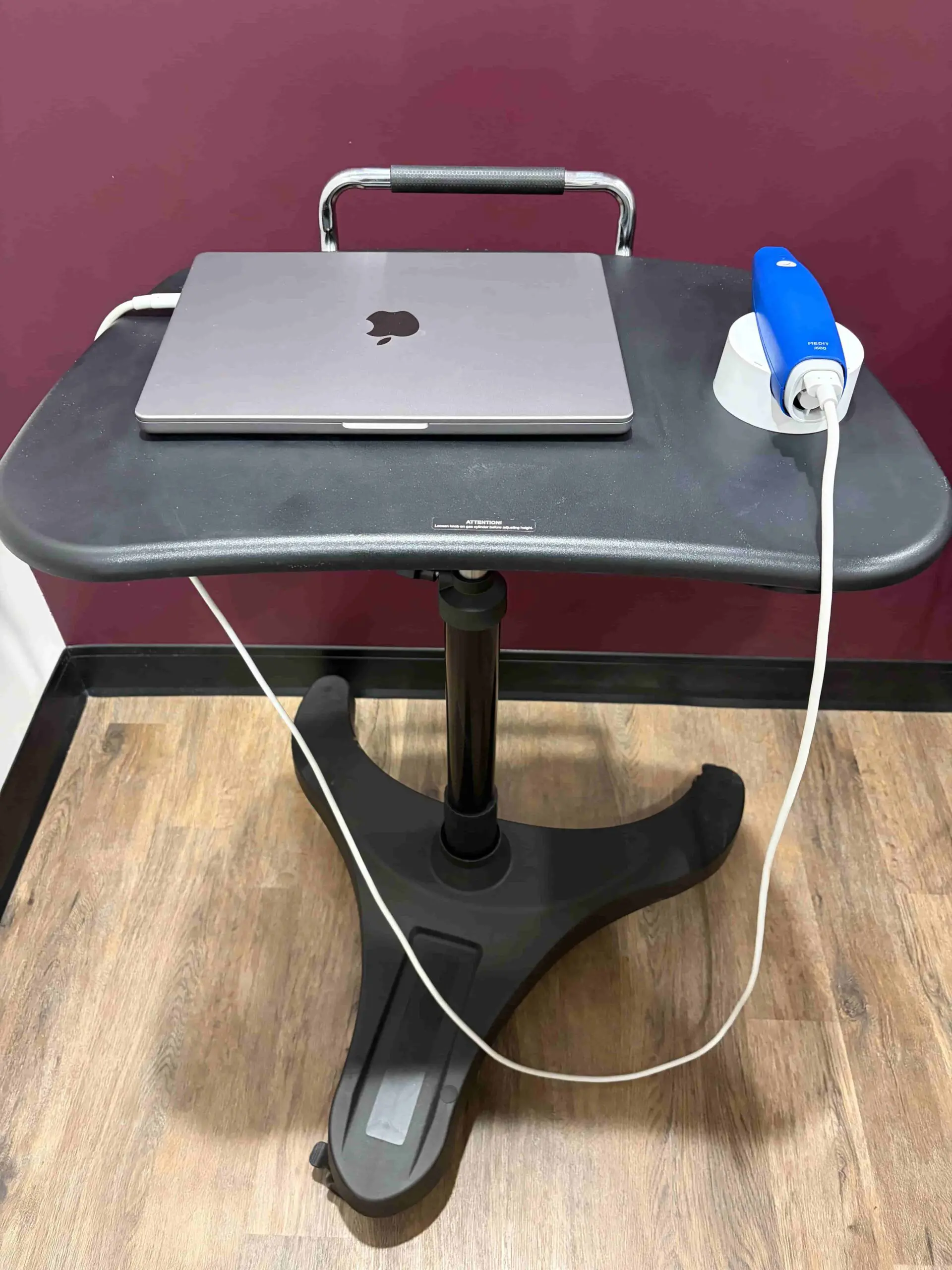 At Holt Orthodontics in Twinsburg, OH, a closed MacBook and blue Medit scanner sit on a rolling desk by a maroon wall and wood floor.