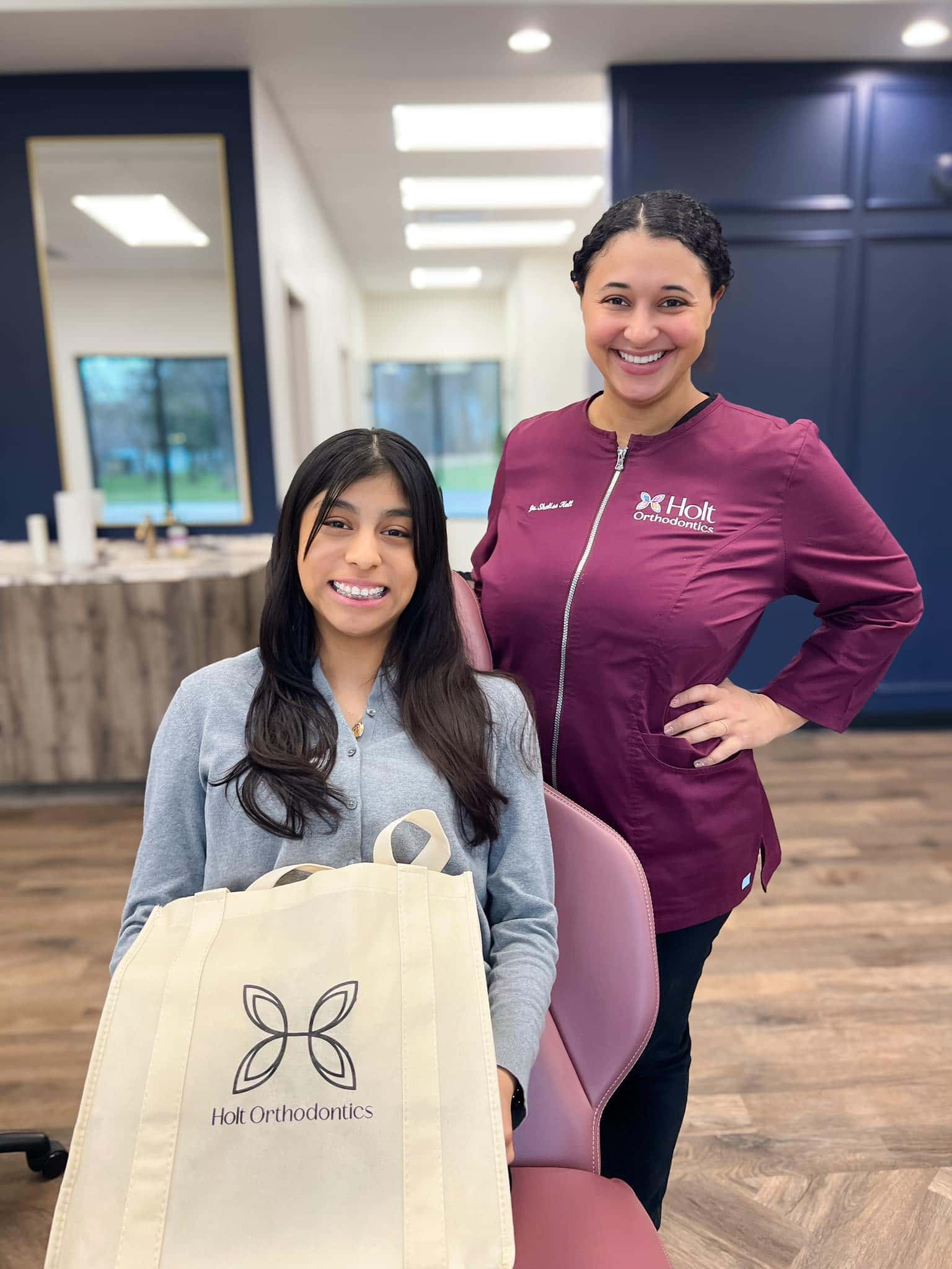 At Holt Orthodontics in Twinsburg, OH, a woman smiles from a dental chair with a Holt Orthodontics tote bag as Dr. Shalise Holt stands beside her.