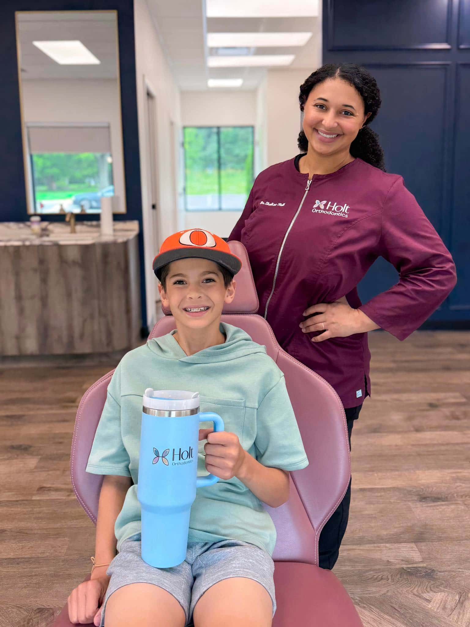 At Holt Orthodontics in Twinsburg, OH, Dr. Shalise Holt and a smiling boy holding a large tumbler pose together in a modern dental office.