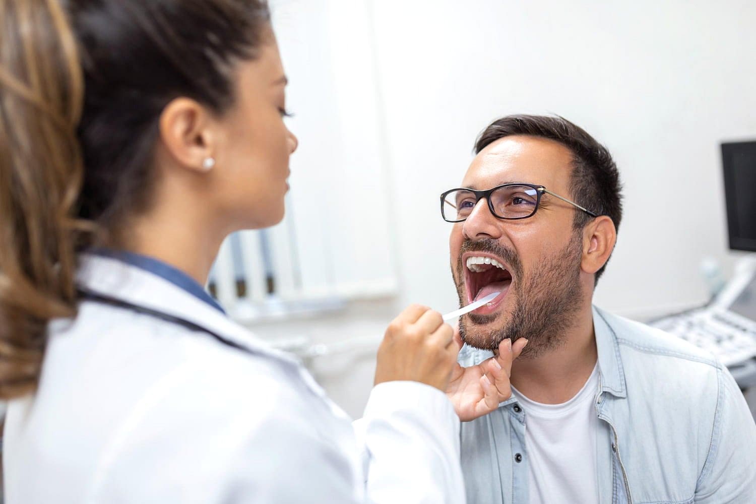 At Holt Orthodontics in Twinsburg, OH, a healthcare professional uses a tongue depressor to examine a male patient’s throat for signs of tongue thrust.