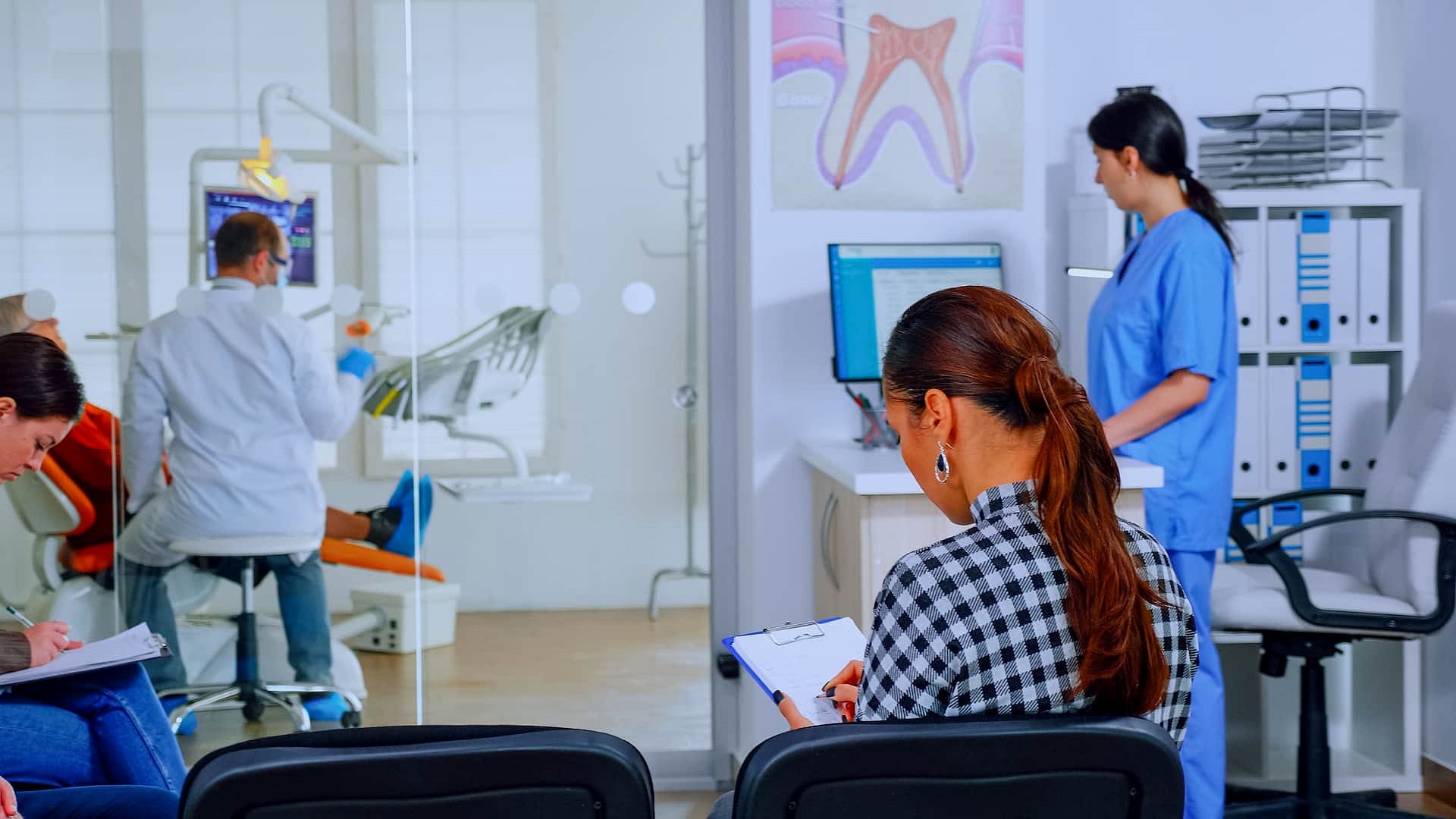 At Holt Orthodontics in Twinsburg, OH, patients complete forms and ask about orthodontic insurance plans in the waiting area, while a dental professional works at a computer and a dentist treats a patient nearby.