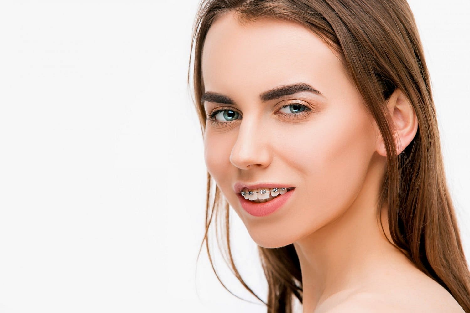 At Holt Orthodontics in Twinsburg, OH, a young woman with long brown hair and light skin smiles over her shoulder, proudly displaying her metal braces as she works to correct her overbite.