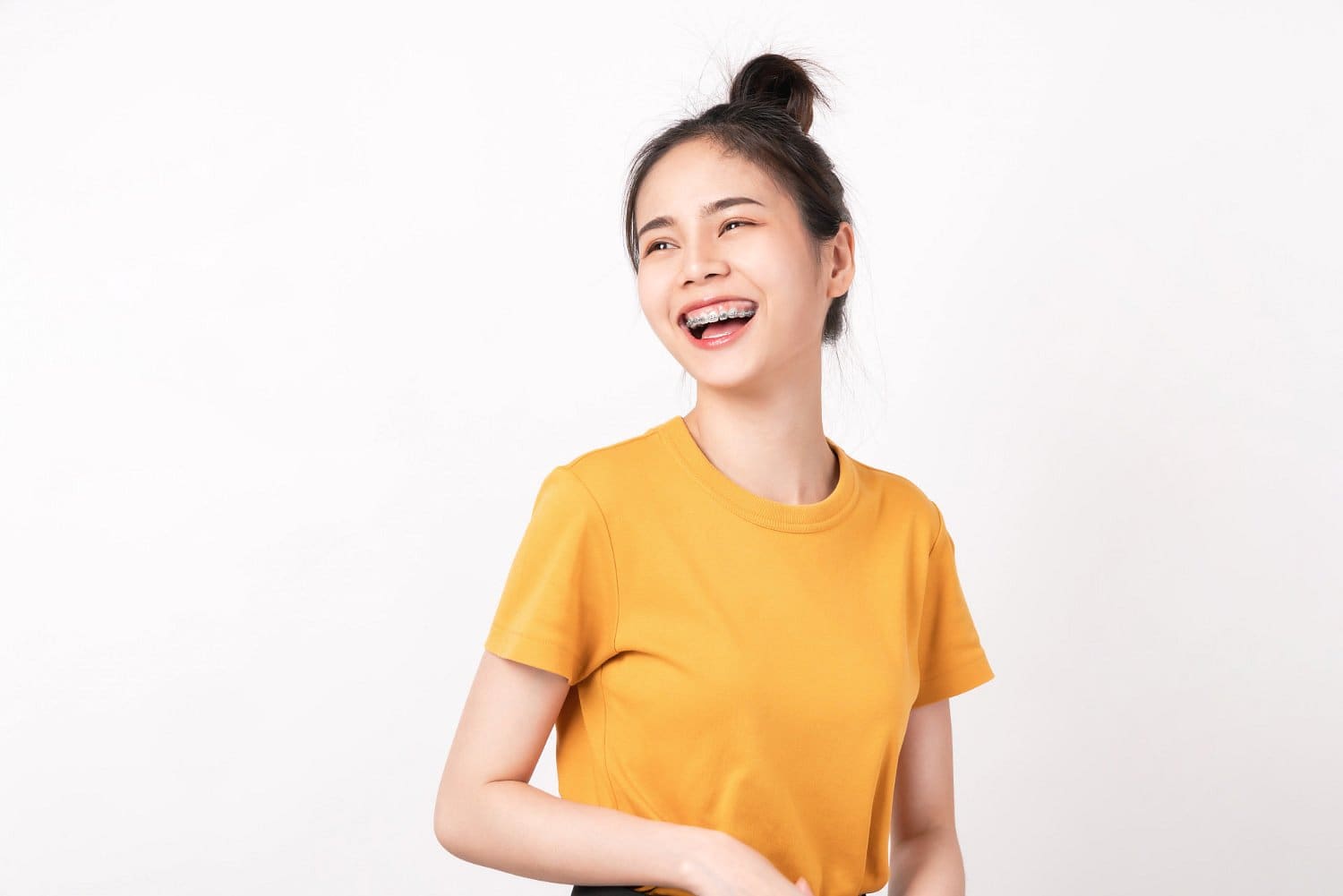 A young woman in a yellow t-shirt, smiling with adult braces, looks slightly to the side against a plain white background at Holt Orthodontics in Twinsburg, OH.