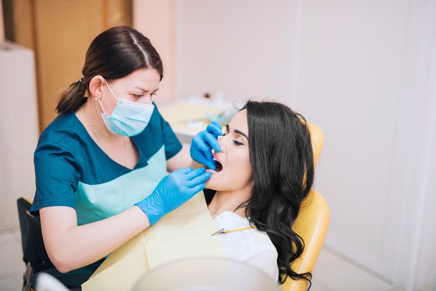 At Holt Orthodontics in Twinsburg, OH, a dentist wearing gloves and a mask examines a patient with braces seated in a yellow dental chair.