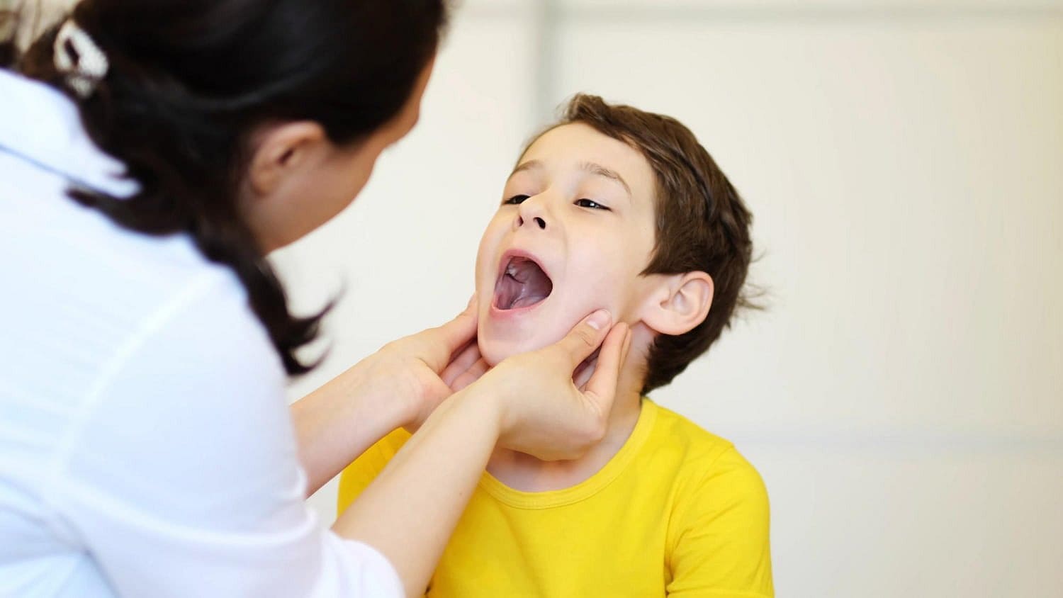At Holt Orthodontics in Twinsburg, OH, a healthcare professional gently holds a child’s jaw to examine their throat while the child with a palatal expander opens wide.