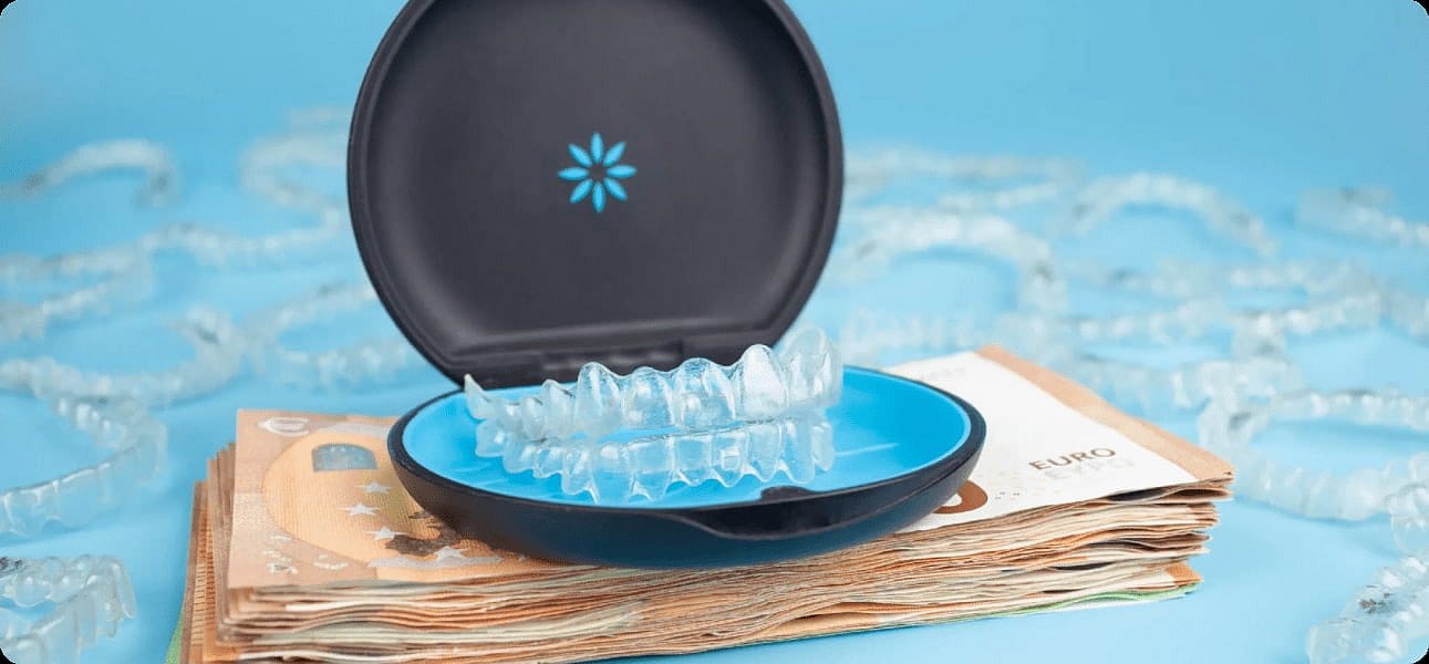 Clear dental aligners in an open case sit atop euro banknotes, illustrating Invisalign cost at Holt Orthodontics in Twinsburg, OH, with additional aligners scattered in the background.