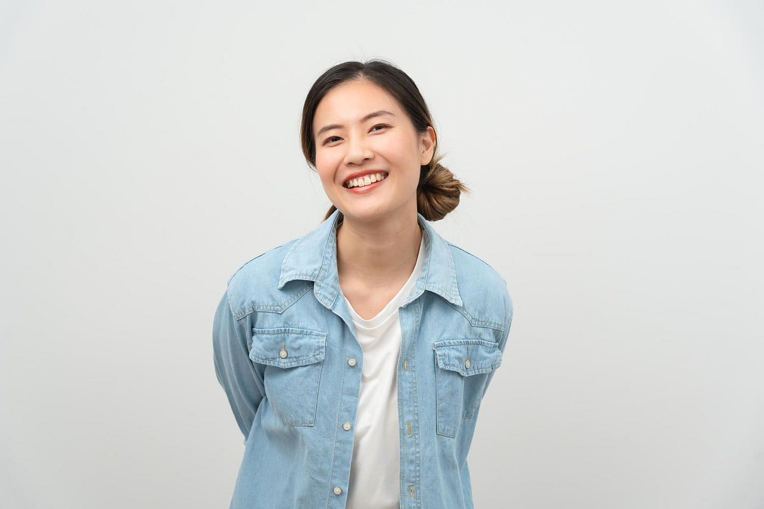 A young woman with dark hair in a ponytail confidently smiles, showing her Invisalign aligners in a light blue denim shirt and white top. This reflects the quality care provided by Holt Orthodontics in Twinsburg, OH.