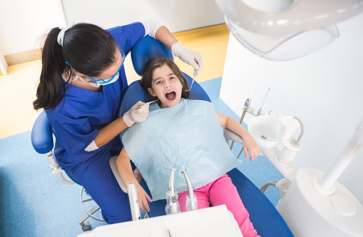 At Holt Orthodontics in Twinsburg, OH, a children’s orthodontist wearing gloves and a mask examines a young girl’s teeth while she sits in the dental chair with a bib.