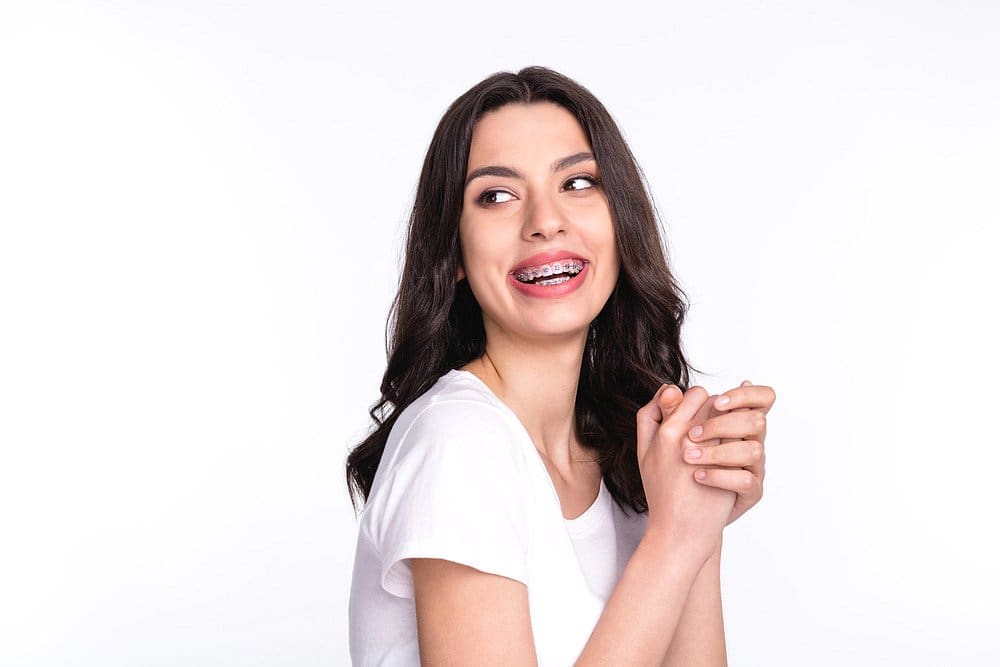 Holt Orthodontics A young woman with long dark hair and a white t-shirt confidently smiles to the side, showing off her metal braces—a perfect example of a smile worth the braces cost at Holt Orthodontics in Twinsburg, OH.
