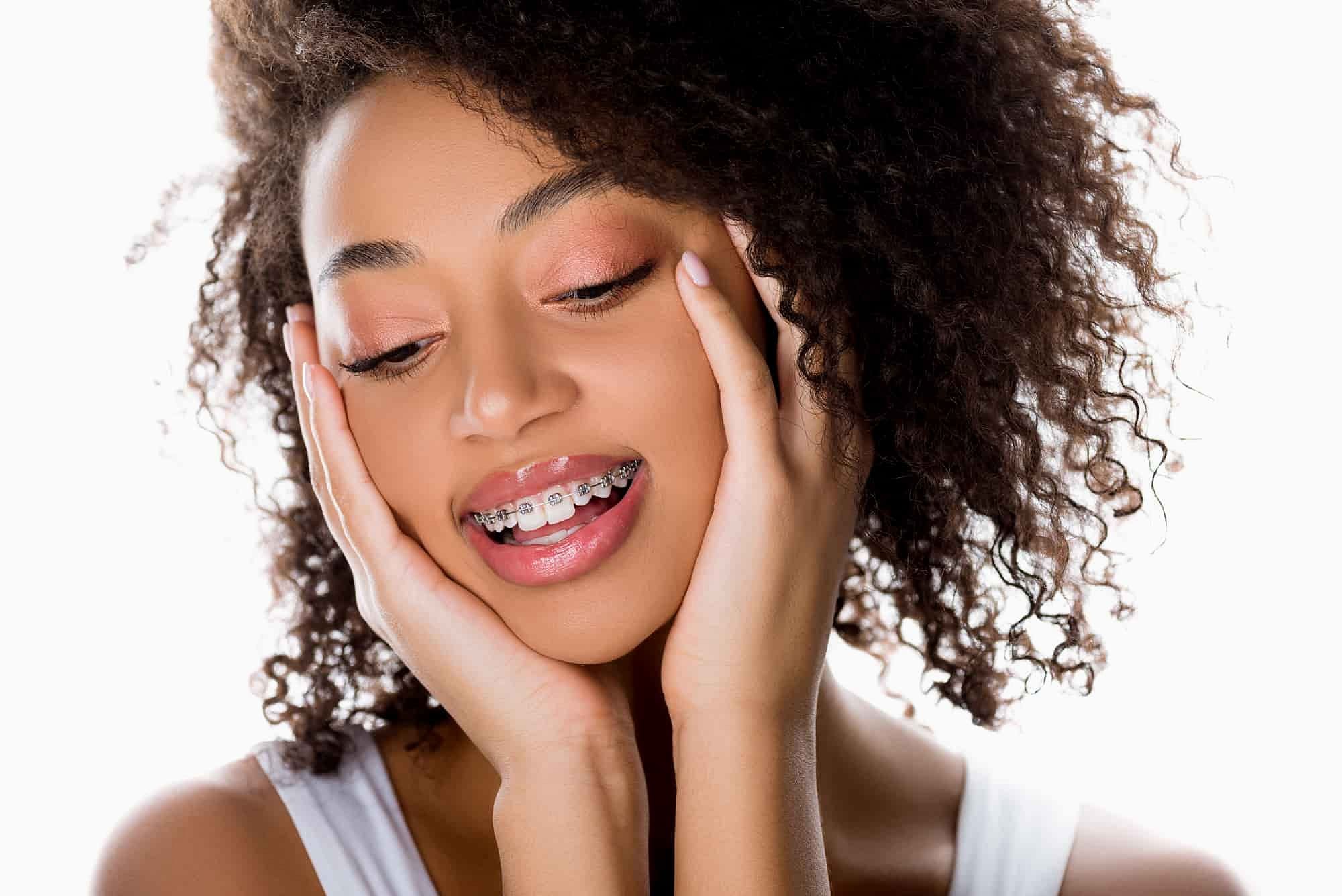 At Holt Orthodontics in Twinsburg, OH, a young woman with curly hair and braces gently smiles, her face resting in her hands against a white background—highlighting one of today’s many types of braces.