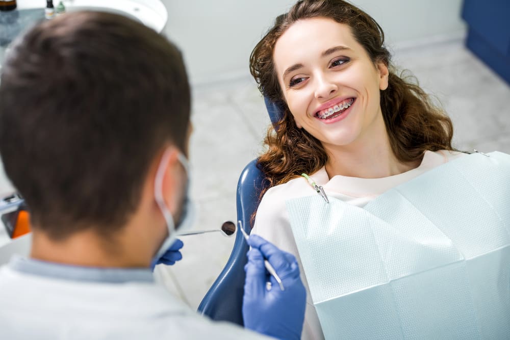 At Holt Orthodontics in Twinsburg, OH, a woman smiles with WildSmiles braces as a dentist in blue gloves examines his teeth.