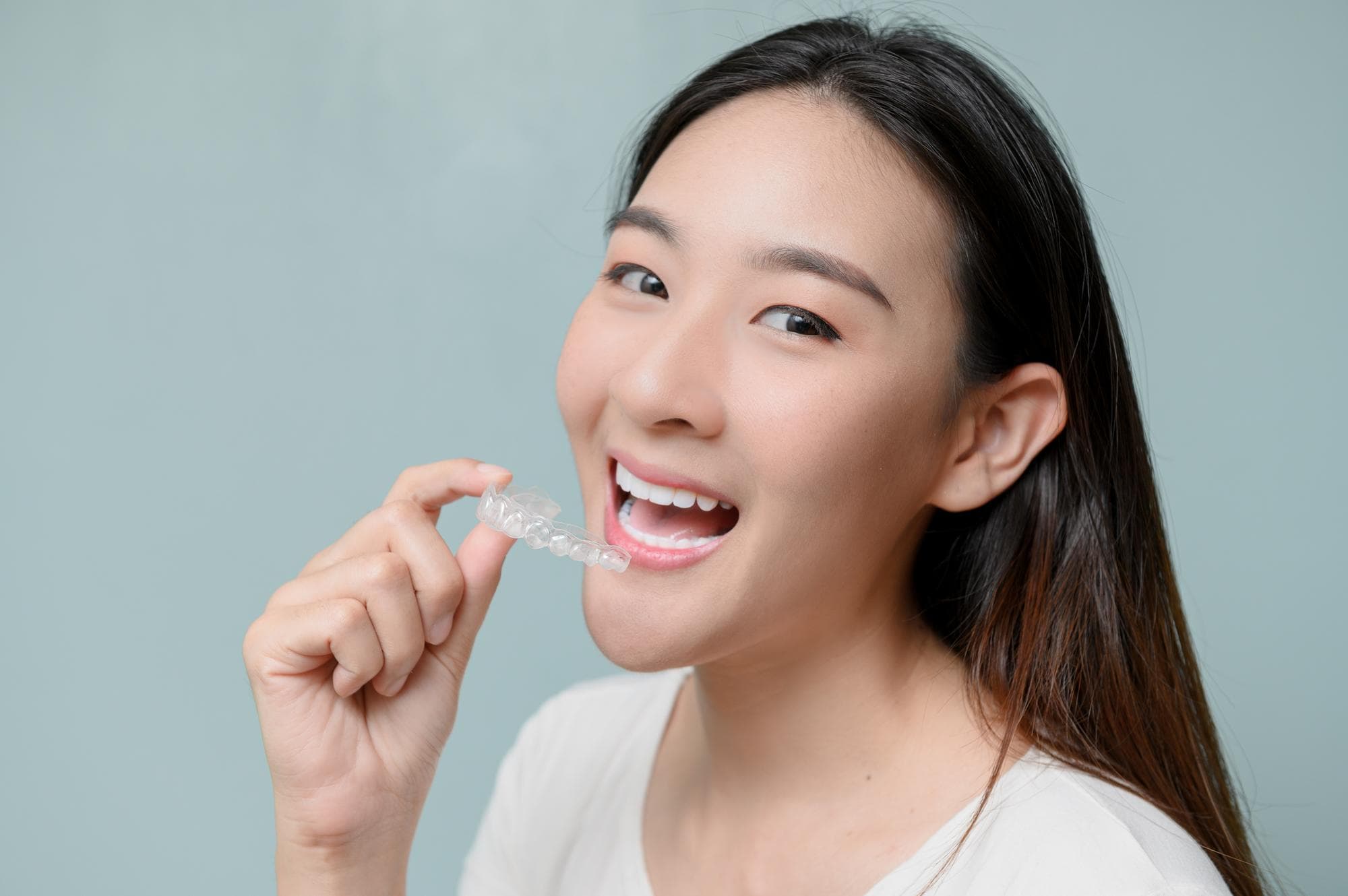 A woman smiles and points to a clear dental aligner near her mouth, showcasing the Invisalign Payment Plan benefits offered by Holt Orthodontics in Twinsburg, OH.