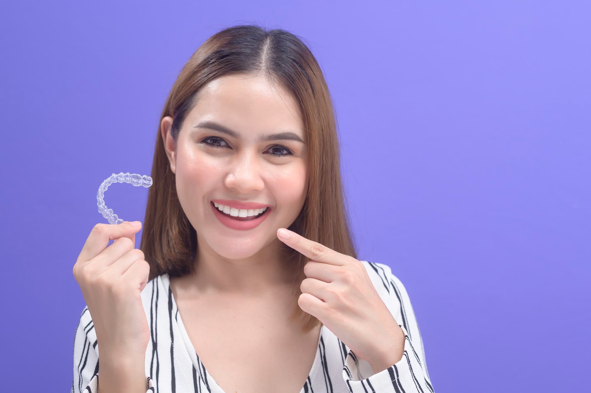 A young woman holds clear aligners, feeling confident after learning about Invisalign vs Braces at Holt Orthodontics in Twinsburg, OH.