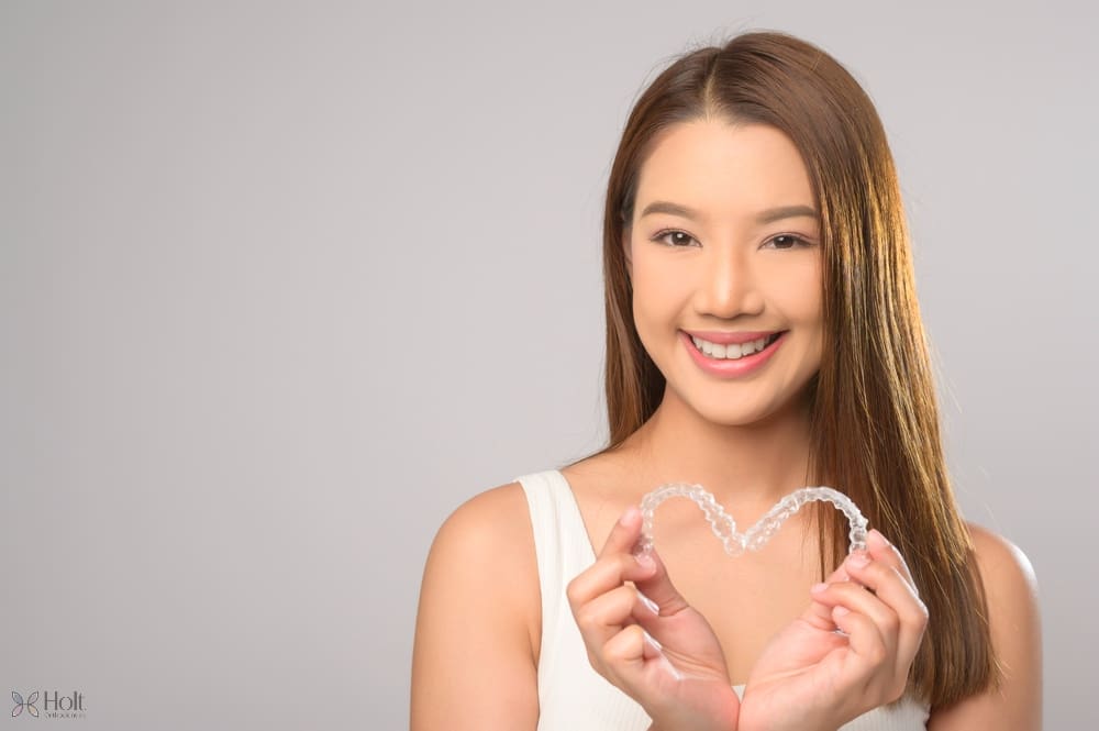 young smiling woman holding invisalign clear aligners white background studio dental - Can Invisalign Fix Overbite in Twinsburg, OH. 