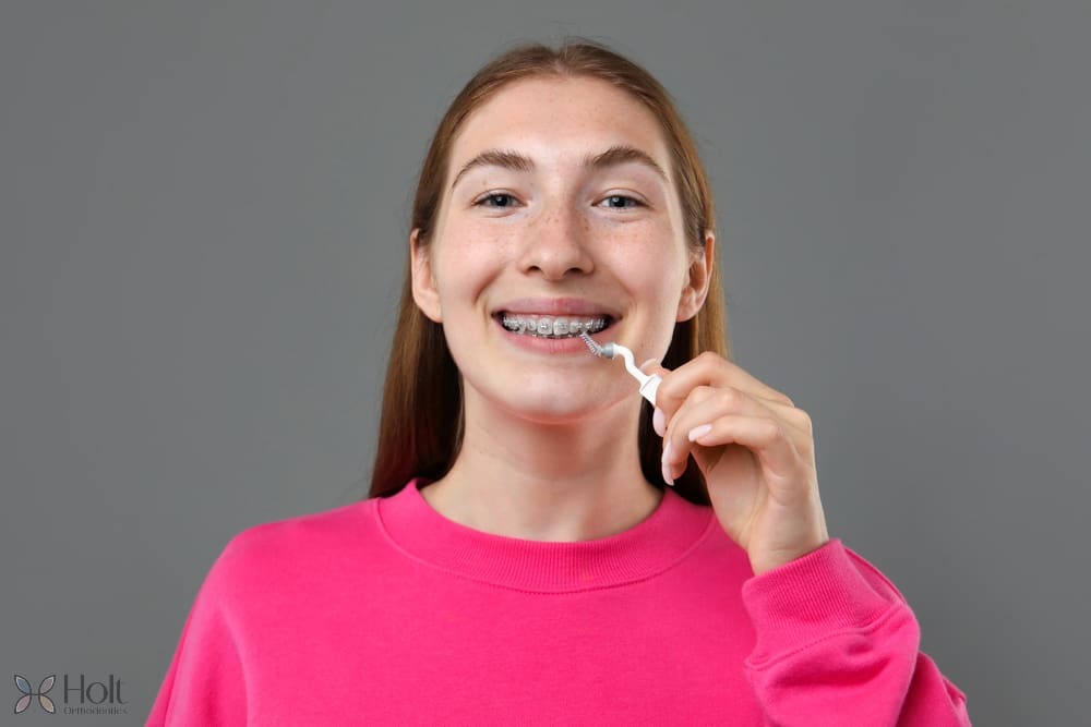 smiling girl metal braces cleaning teeth interdental brush grey background - How to Floss with Braces in Twinsburg, OH